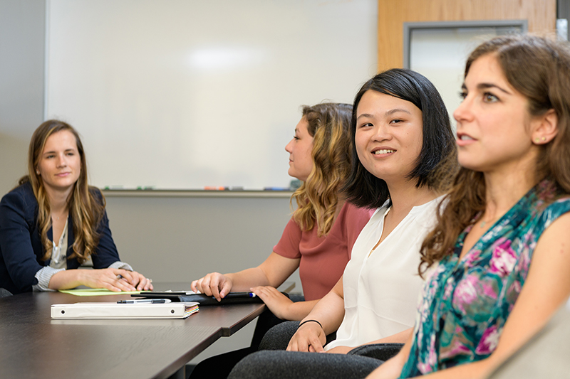 Four graduate students sit around a table in a meeting inside a conference room.